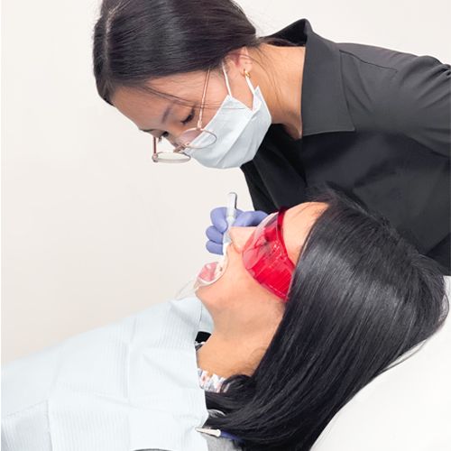 Esthetician in black smock applying teeth whitening gel to a female client's teeth.