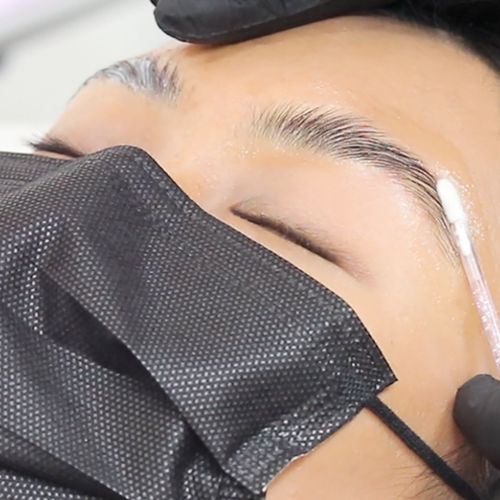 Brow lamination adhesive being applied to end of client's eyebrow with the tip of a cotton swab.