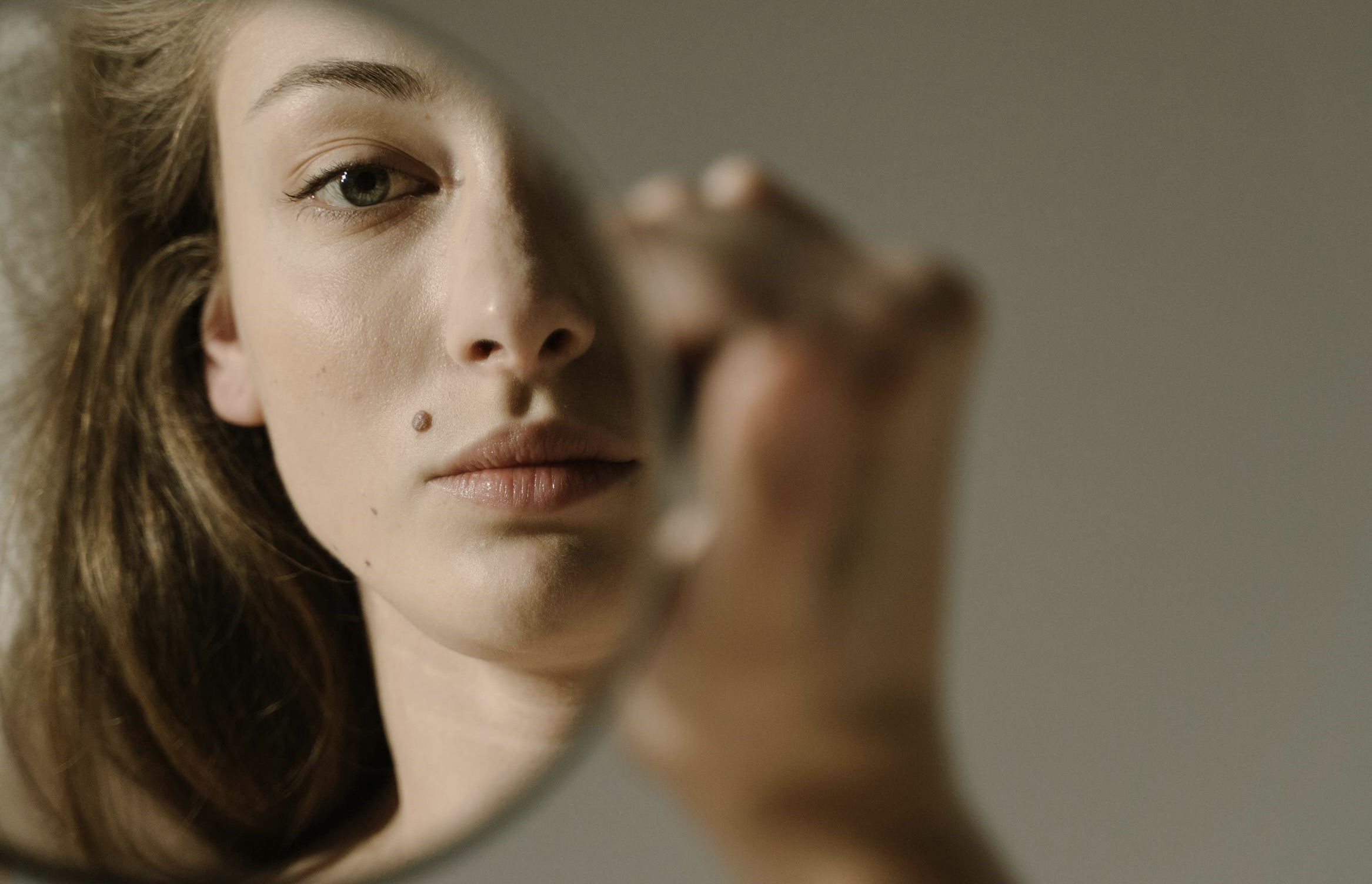 oman looking in mirror and wondering if she should dermaplane at home or let someone with a beauty school in Winnipeg, Manitoba diploma do it