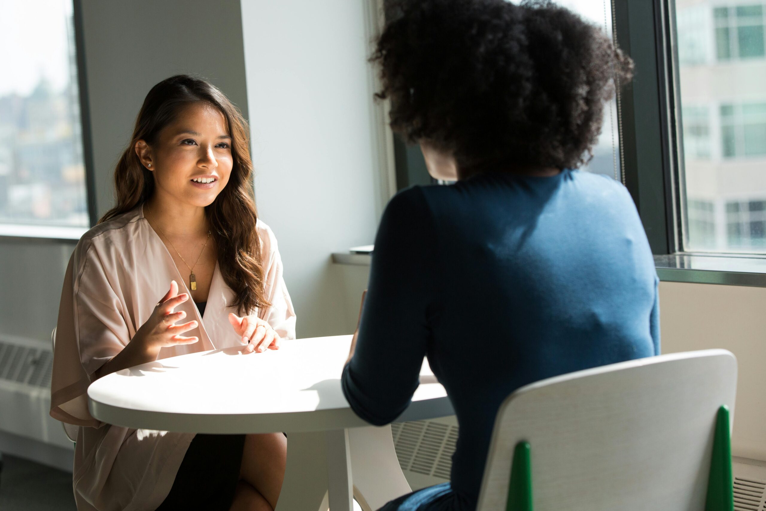 Two estheticians chatting at a networking event, each confidently sharing their mini bios — answering the question, “How Do I Introduce Myself as an Esthetician?” Possibly an ipromptu job interview.