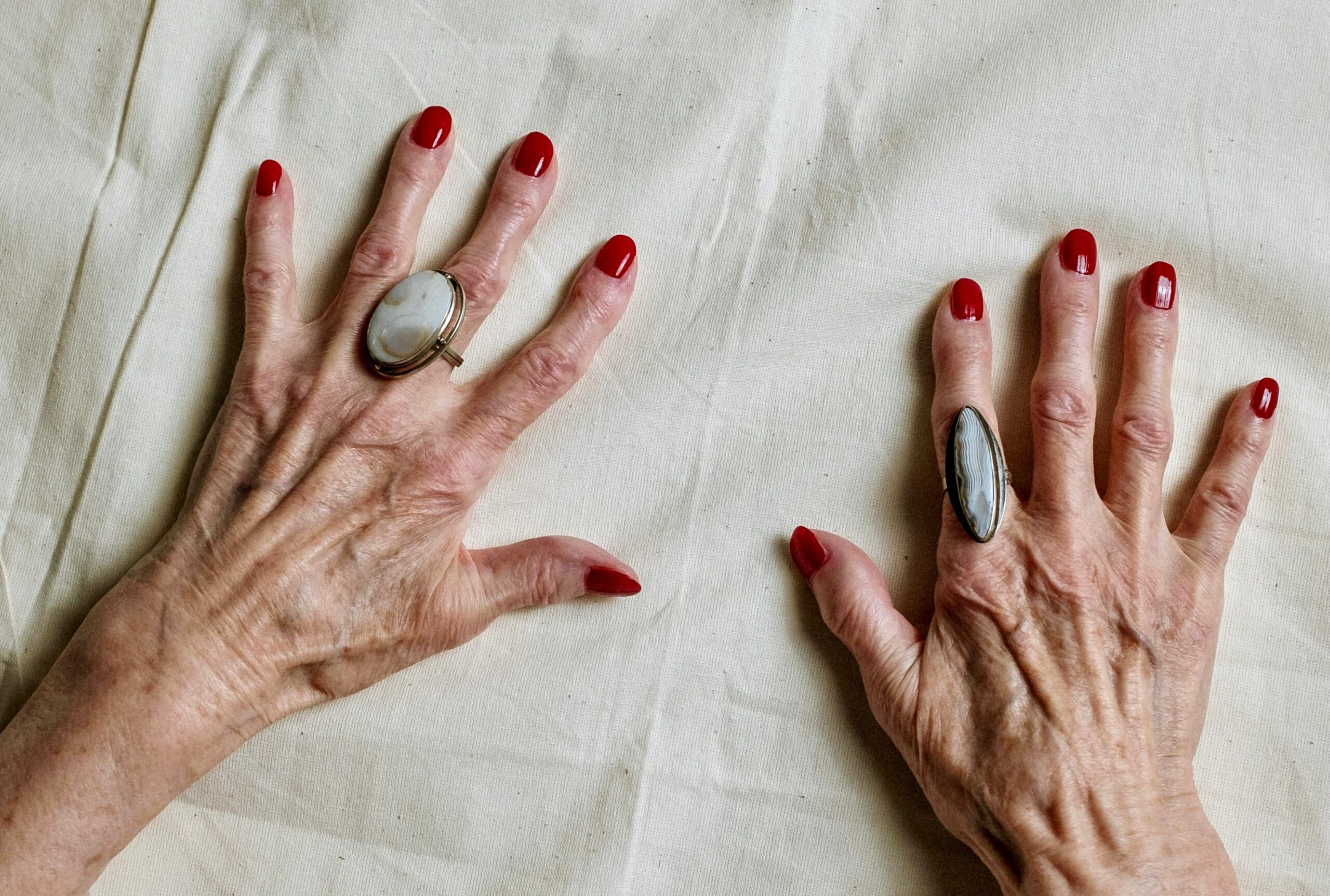 A nail technician program model displays a clean, professional shellac manicure in deep cherry, cured to a mirror-like shine.