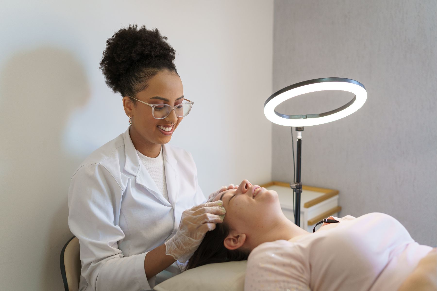 Smiling esthetician performing a facial treatment under a ring light, showing behind-the-scenes content for social media for estheticians
