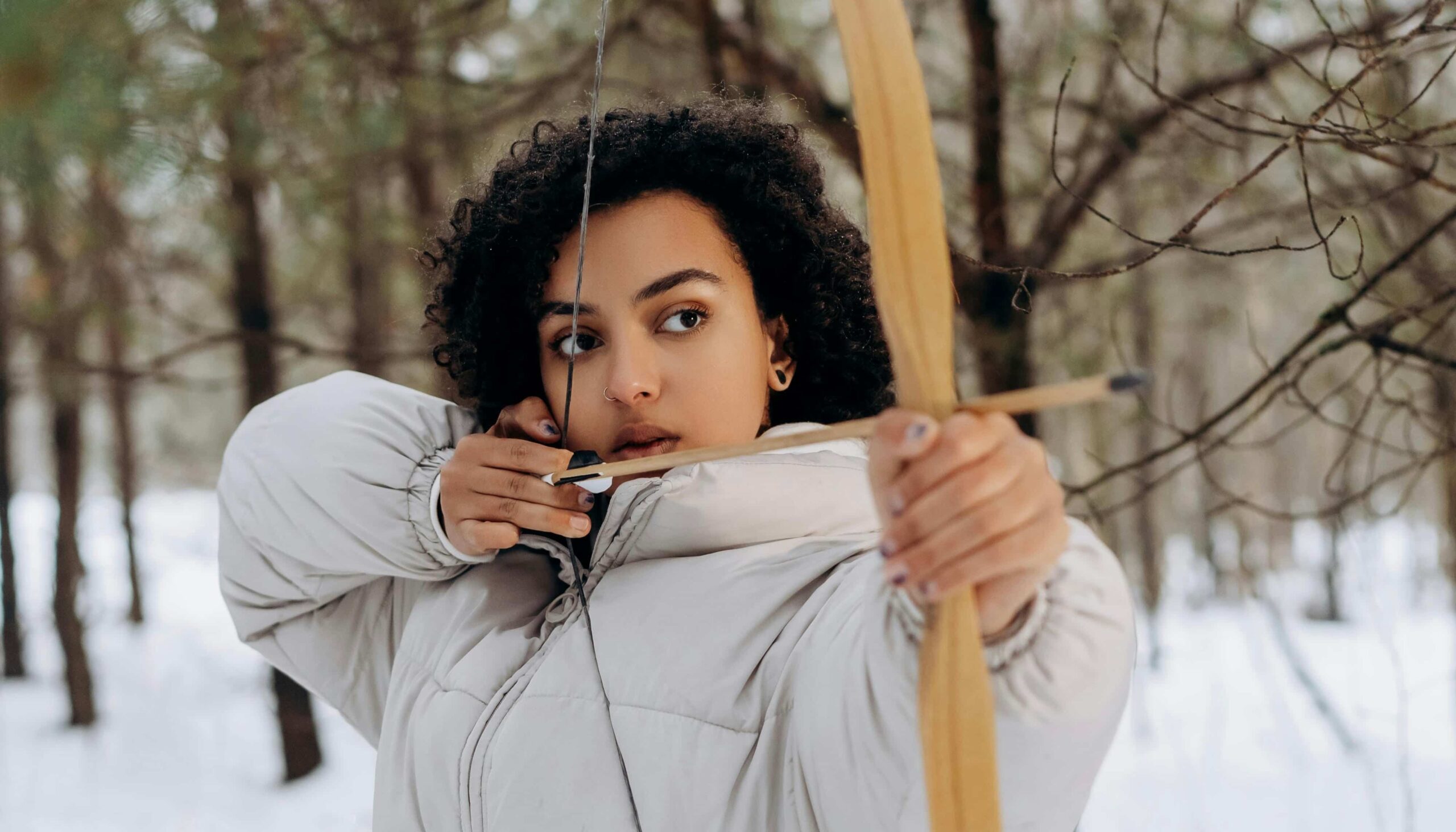 Focused archer aiming her bow in the forest, representing intentional marketing with a goal instead of scattered promotion.